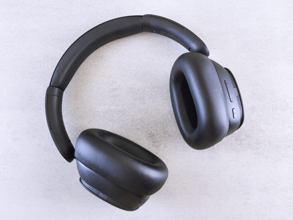 Top view of modern black over-ear wireless headphones on a light textured surface.